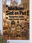 Zwarte raamsticker Welkom Sint en Piet met tekst 'Vergeten jullie mijn huisje niet?' op raam met gezellige woonkamer op achtergrond