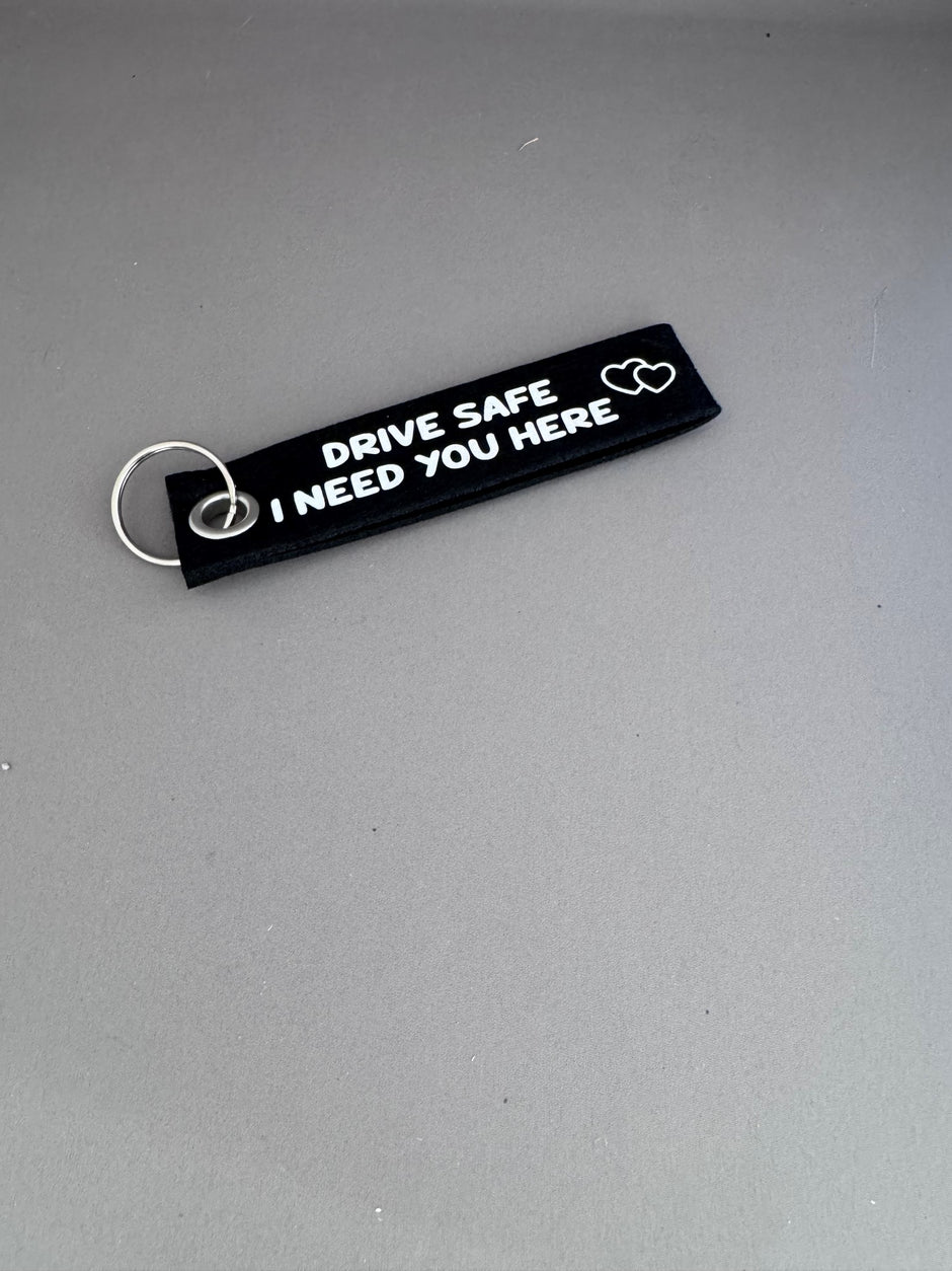 Zwarte viltsleutelhanger met witte tekst 'Drive Safe I Need You Here' – persoonlijk cadeau voor rijbewijs of nieuwe auto van Shop V-Ric
