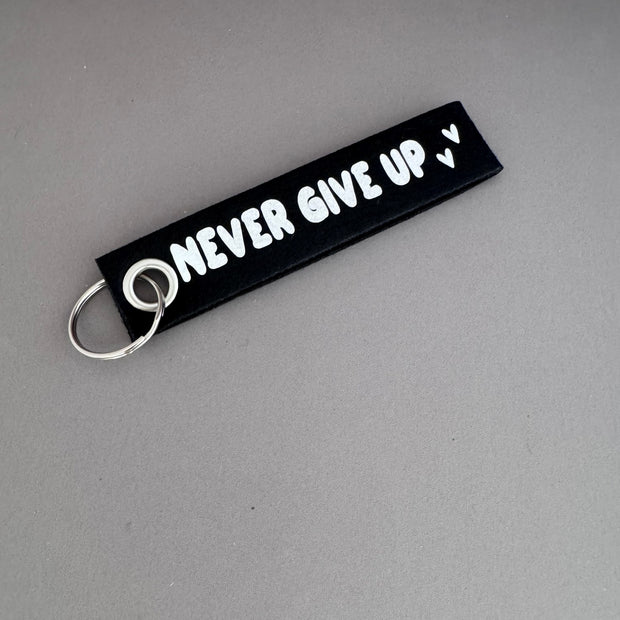 Zwarte viltsleutelhanger met witte tekst 'Never Give Up' – motiverend cadeau van Shop V-Ric

